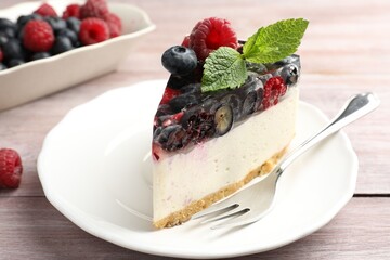 Piece of delicious cheesecake with berries, mint and fork on wooden table, closeup