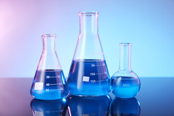 Glass flasks with blue liquid on mirror surface against color background