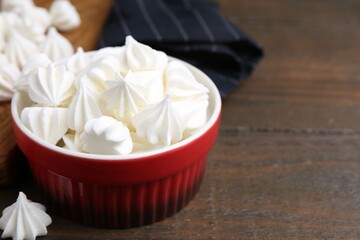 Delicious meringue cookies in bowl on wooden table, closeup. Space for text
