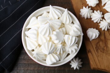 Delicious meringue cookies in bowl on wooden table, top view