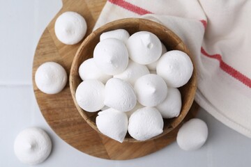 Delicious meringue cookies in bowl on white tiled table, top view