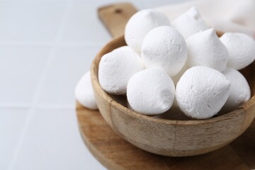 Delicious meringue cookies in bowl on white tiled table, closeup. Space for text