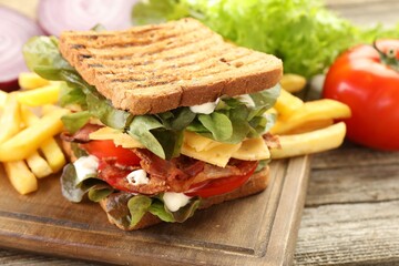 Tasty sandwich served with french fries on wooden table, closeup