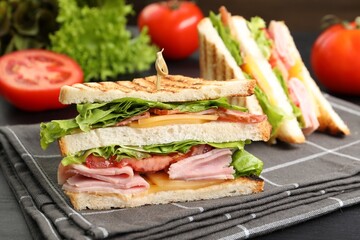 Tasty sandwiches with ham, bacon, cheese and vegetables on black wooden table, closeup