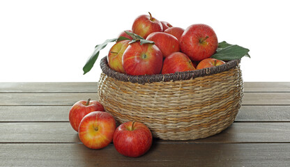 Fresh apples in wicker basket and green leaves on wooden table against white background