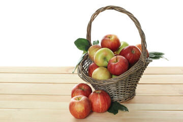Fresh apples in wicker basket and green leaves on wooden table against white background