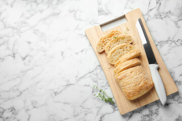 Cut crispy ciabatta, knife and thyme on white marble table, top view. Space for text