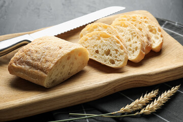 Pieces of fresh ciabatta, knife and wheat ears on black table, closeup