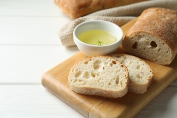 Fresh crispy ciabattas and oil with rosemary on white wooden table, closeup. Space for text