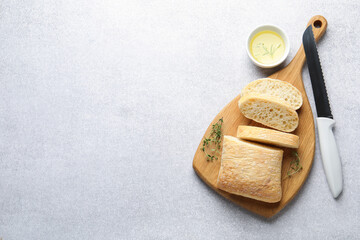 Fresh crispy ciabatta, oil, herbs and knife on grey table, flat lay. Space for text