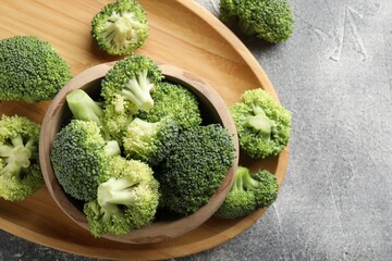 Fresh raw broccoli in bowl on gray textured table, top view