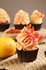 Delicious cupcake with branch with red leaves on table against grey background, closeup. Autumn atmosphere