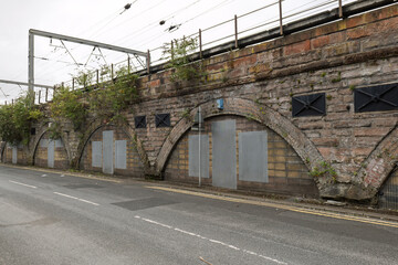 Railway viaduct storage arches sealed with doors and metal panels beneath active train tracks, highlighting urban decay, history, and industrial architecture.