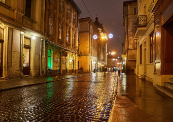 Wet cobblestone street reflecting lights in a historic European city at night.