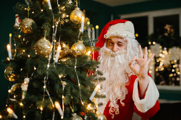 Santa claus winking and gesturing ok near christmas tree