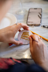 Woman painting small round canvas with fine brush at table