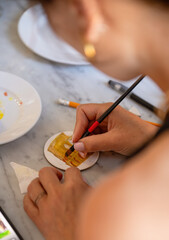 Woman painting small round canvas with fine brush at table