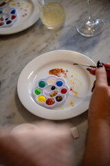 Hand mixing paint with brush on white plate and colorful palette