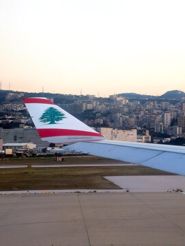 Middle East Airlines aircraft wing with Lebanese cedar emblem during takeoff and landing in Beirut, Lebanon, with urban cityscape in the background