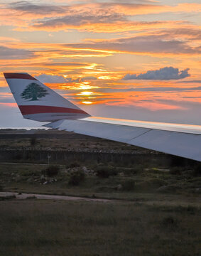 Middle East Airlines aircraft wing with Lebanese cedar emblem during takeoff and landing in Beirut, Lebanon, with dramatic sunset sky in the background