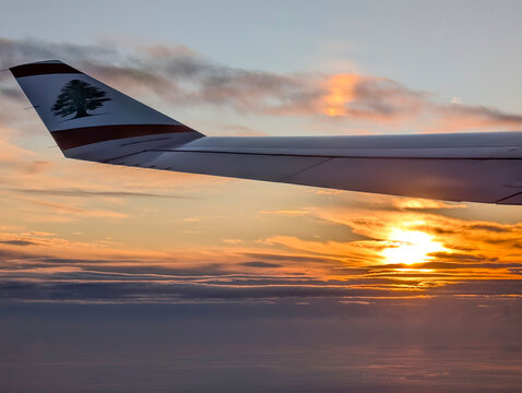Middle East Airlines aircraft wing with Lebanese cedar emblem during takeoff and landing in Beirut, Lebanon, with dramatic sunset sky in the background