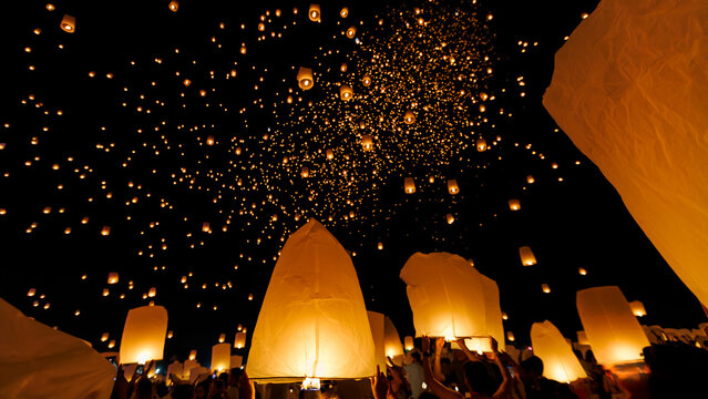 A breathtaking low-angle shot of the Yee Peng festival in Chiang Mai, showing hundreds of illuminated sky lanterns (Khom Loi) ascending into the dark night sky.

