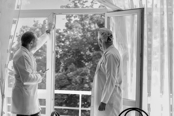 A black-and-white photo of two doctors chatting after a surgery near an open window. Colleagues. Medicine and health.