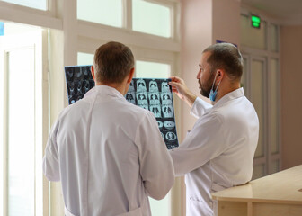 Two doctors holding and looking at MRI or CT scans with human organs in the light. Concept of medical diagnostics, radiology, examination and health research.