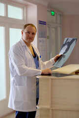 Caucasian doctor in white coat holding MRI or CT scan images at the reception desk. Concept of treatment, medicine and health.