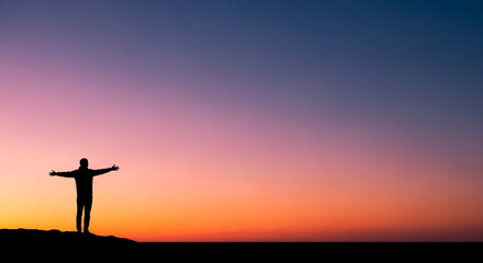 Silhouette of a person standing with arms outstretched against a vibrant sunset sky, embodying freedom, peace, and the beauty of nature