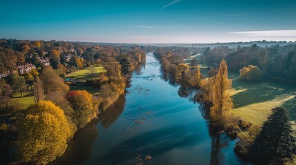Obraz premium The river winds gently between trees, where the river reflects autumn colors. Houses line the river, while the river sparkles under the sunlight and the vibrant trees sway.