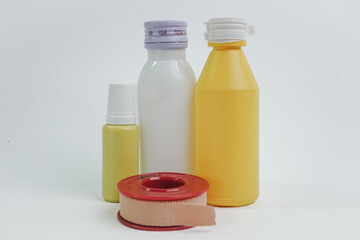An assortment of healthcare items, including a white bottle with a purple cap, a yellow bottle, a small dropper bottle, and a roll of skin-colored medical tape, symbolizing comprehensive first aid.