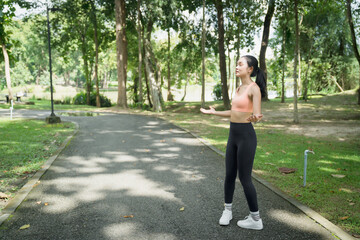 Woman standing in a lush green park with eyes closed and arms open, breathing deeply and meditating to find inner peace, balance and calm in nature-filled summer daylight