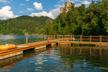 Scenic view of a wooden pier stretching over calm lake water with a historic castle tower visible...