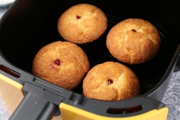Freshly baked muffins in air fryer on grey textured table, closeup