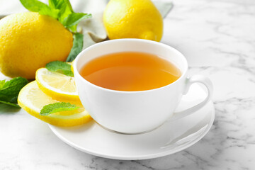 Aromatic tea in cup with lemons and mint on white marble table, closeup