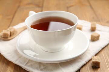 Aromatic black tea in cup and sugar cubes on wooden table, closeup