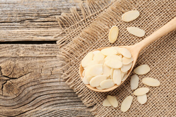 Fresh almond flakes in spoon on wooden table, above view. Space for text