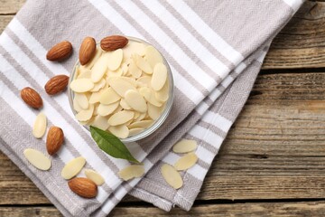 Fresh almond flakes and whole nuts on wooden table, top view. Space for text