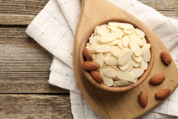 Fresh almond flakes and whole nuts in bowl on wooden table, top view. Space for text
