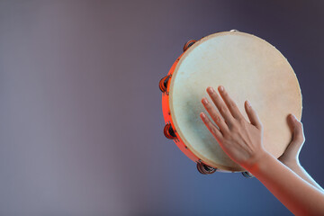 Woman playing tambourine on grey background, closeup. Space for text