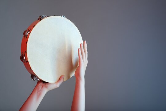 Woman playing tambourine on grey background, closeup. Space for text