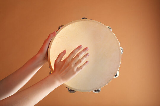 Woman playing tambourine on brown background, closeup