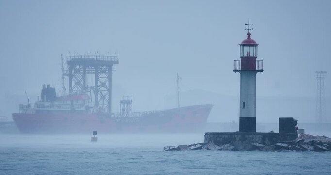 Misty Harbor Scene With Red Cargo Ship And Lighthouse on the coast In Fog and Rain At Dawn stormy weather Varna sea port, Bulgaria