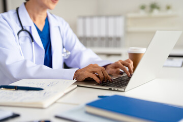 Doctor working in office, using a laptop to access patient records on system. Mature female physician using modern technology in her practice.
