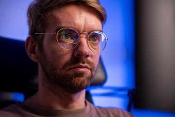 Business man trader wearing glasses looking at computer screen with trading charts reflecting in...