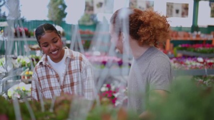 Young diverse couple having fun while shopping for plants at a local nursery. The smiling man and woman are browsing through hanging flower baskets, enjoying their date together outdoors