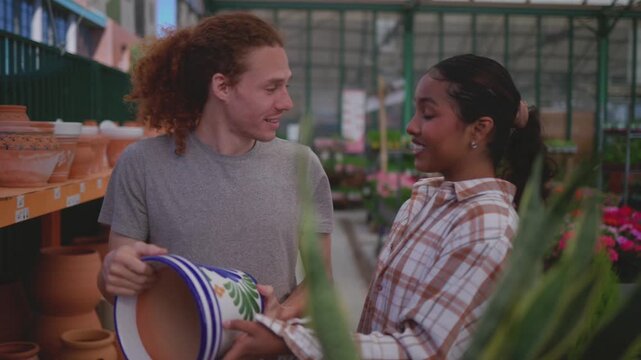 Happy young diverse couple talking and laughing while choosing a ceramic flower pot at a local plant nursery, enjoying their time together shopping for gardening supplies and home decor - Powered by Adobe