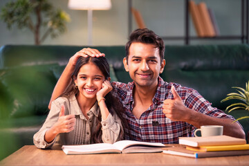 Indian Father helping daughter study from textbook, family learning moment at home