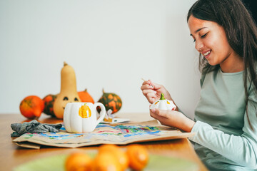 Female kid painting a pumpkin on a cup for an halloween party fest - Holidays and art concept - Main focus on face